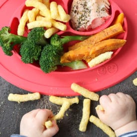 Baby playing with food next to a red plate with baby led weaning lunch.