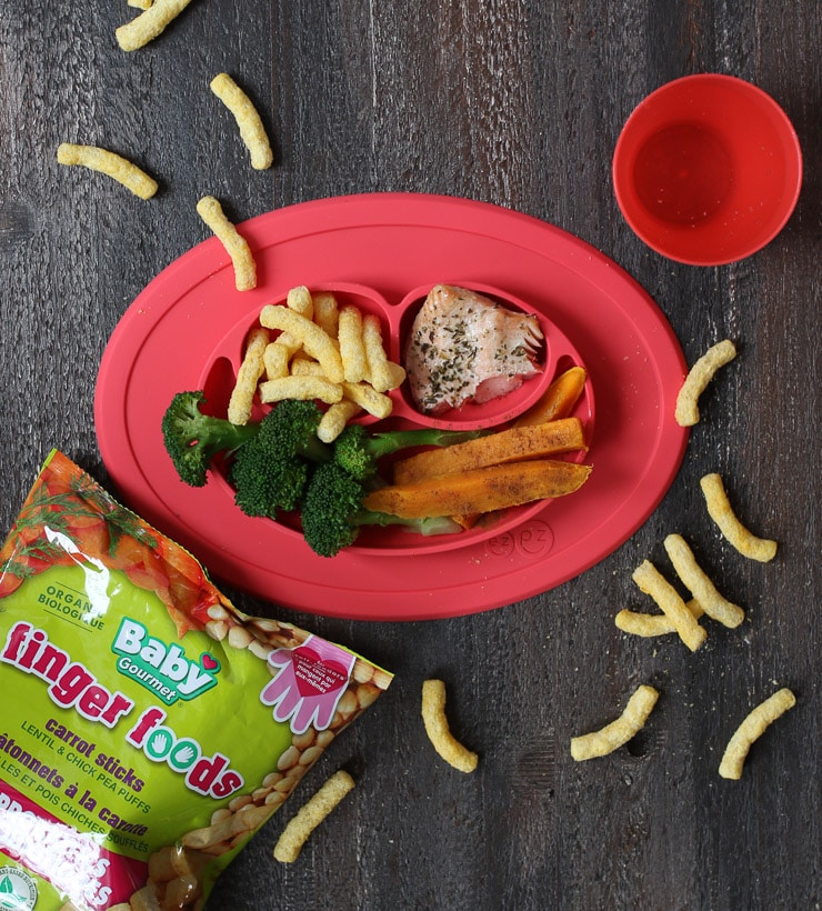 Baby led weaning lunch on a red plate containing broccoli, sweet potato, salmon and baby gourmet carrot sticks.