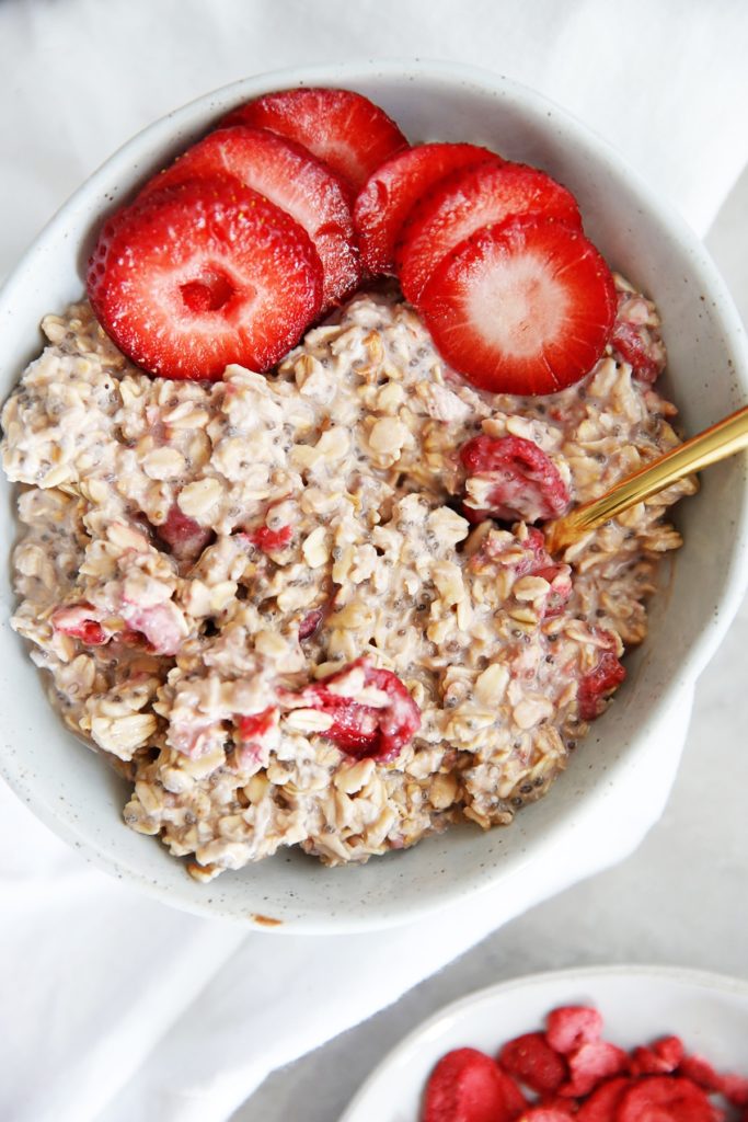 Strawberry overnight oats in a white bowl with a gold spoon from family meal plan.