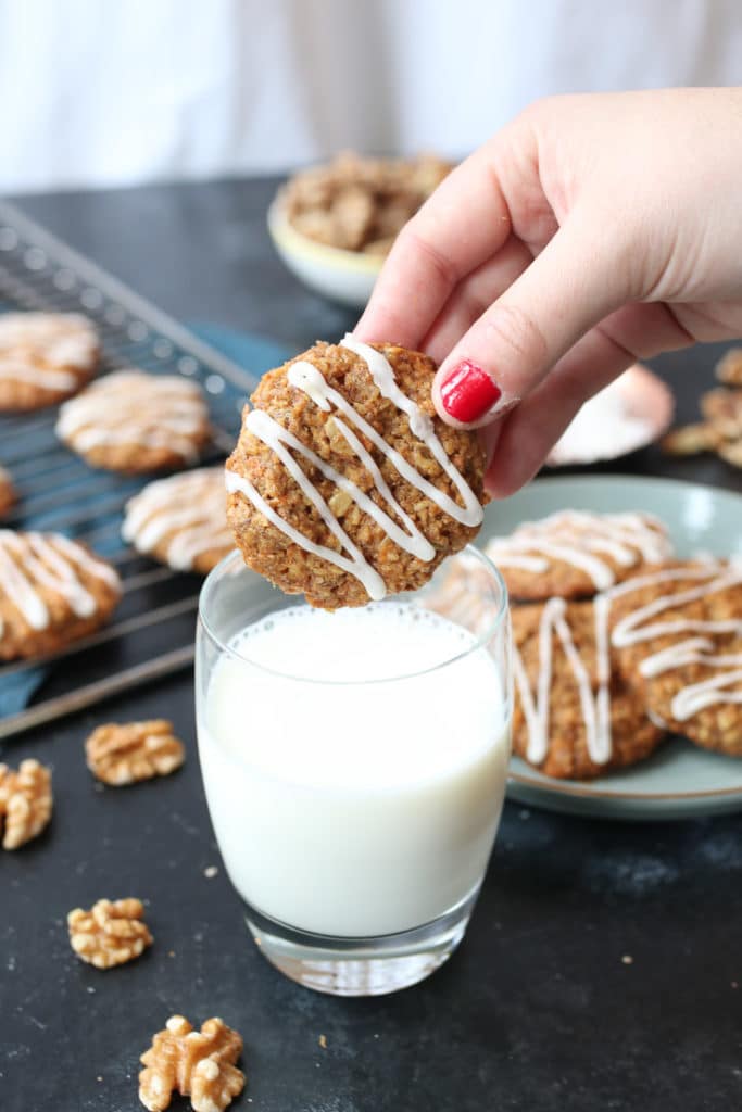 Hands dipping vegan carrot cake lactation cookies in a glass of milk.