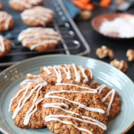 Pile of vegan carrot cake lactation cookies on a teal plate with cookies on a rack in the background.