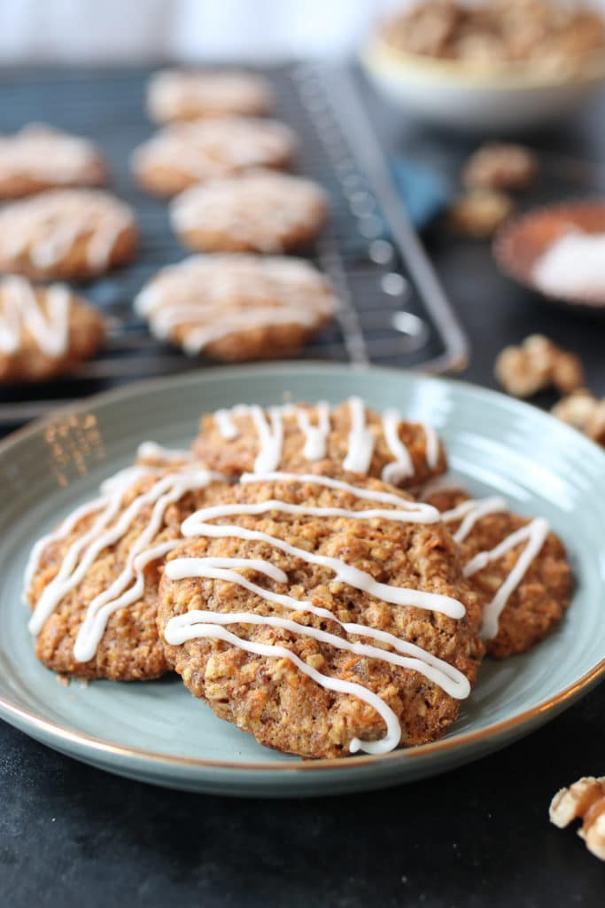 Pile of vegan carrot cake lactation cookies on a teal plate with cookies on a rack in the background.