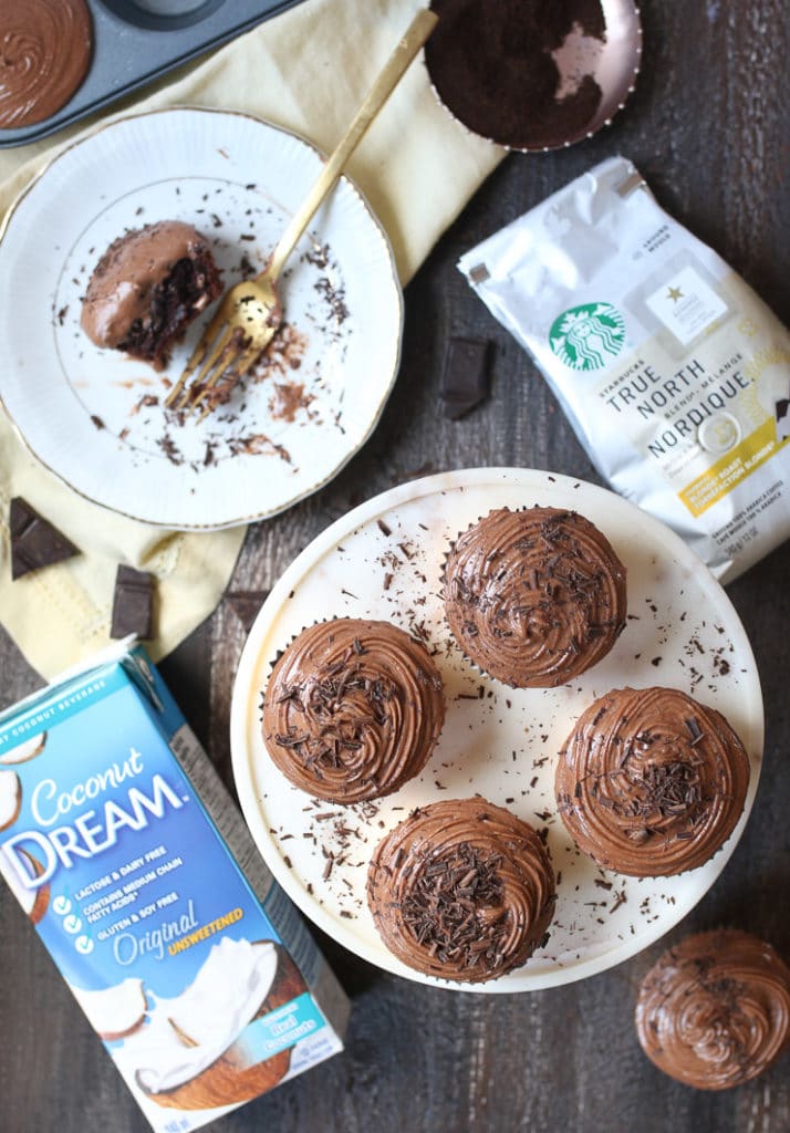 Mocha latte cupcakes on a white plate sprinkled with chocolate savings next to coconut milk and Starbucks coffee.