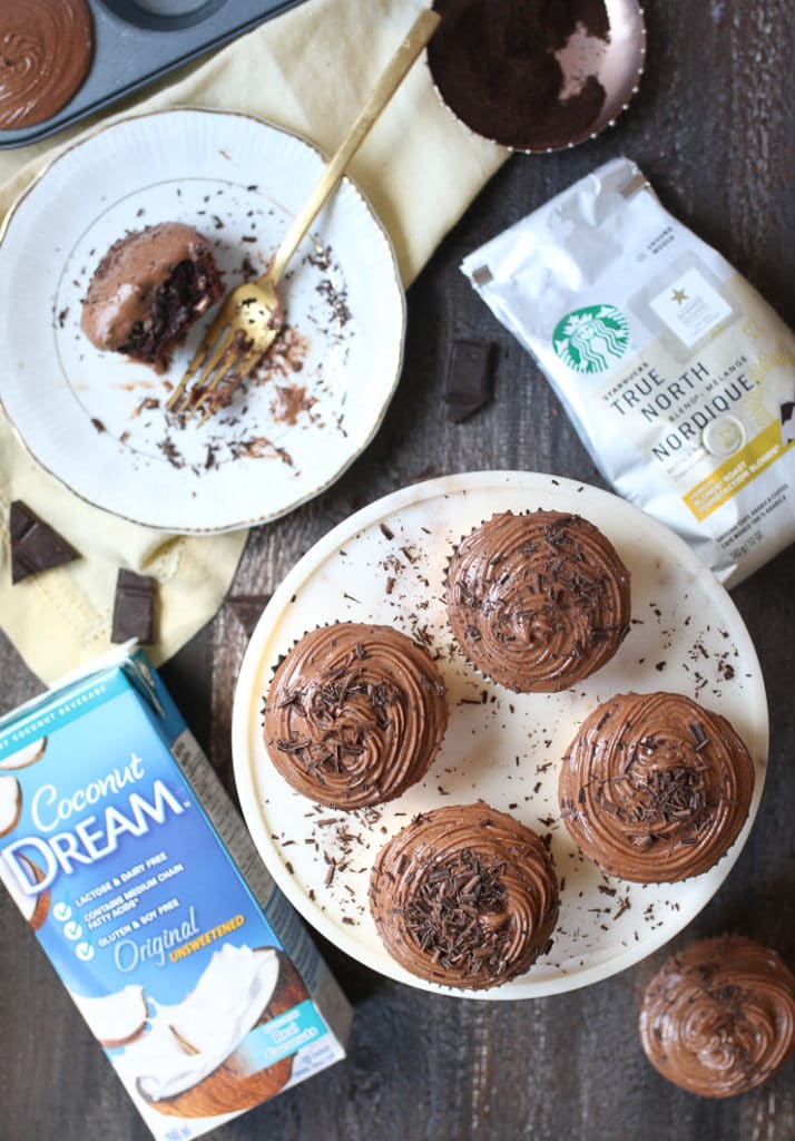 Mocha latte cupcakes on a white plate sprinkled with chocolate savings next to coconut milk and Starbucks coffee. 