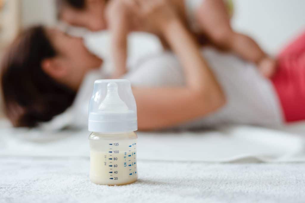 Mom picking up baby next to a baby bottle.