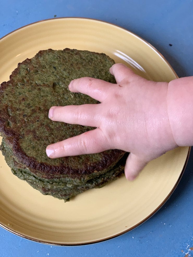 Baby's hand on a stack of spinach and avocado green pancakes.