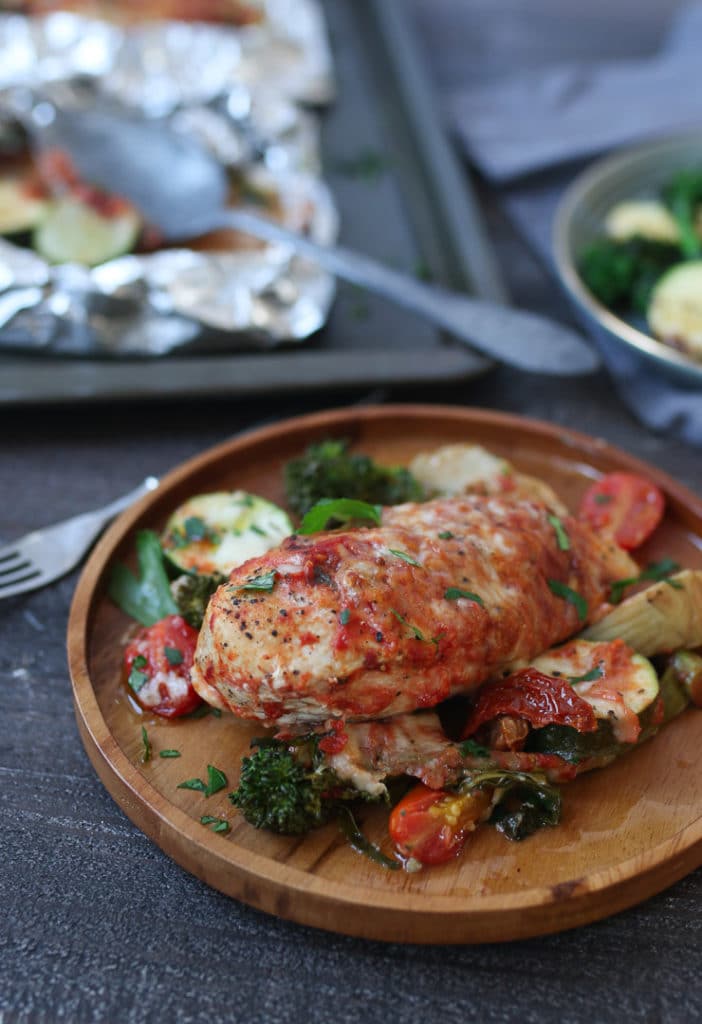 Baked chicken parmesan foil pack dinner on a wooden plate with vegetables.