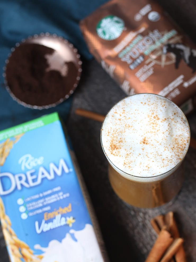 Horchata latte in a tall glass topped with rice milk foam next to a bag of Starbucks coffee and rice milk.