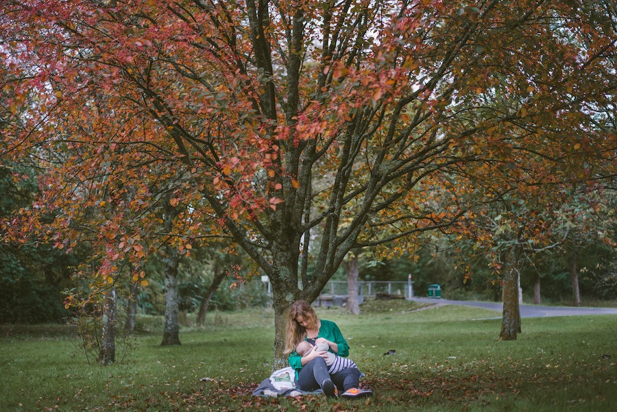 Mother breastfeeding baby in a park.