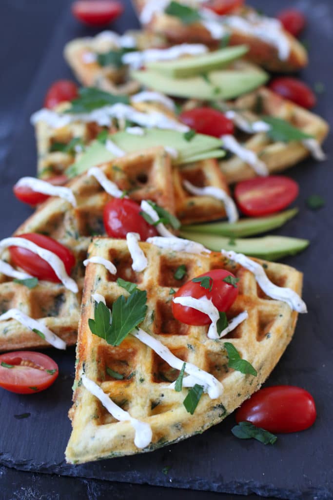 a platter of egg and cheese waffles topped with cherry tomato and parsley
