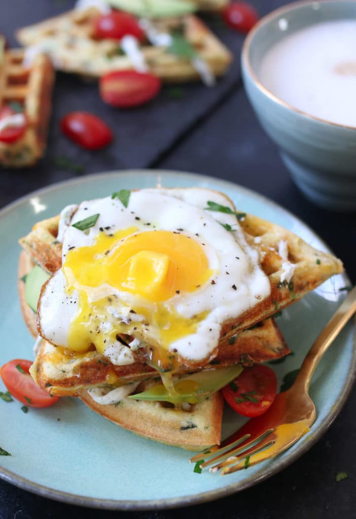 three savory protein waffles stacked on a blue plate topped with a runny egg 