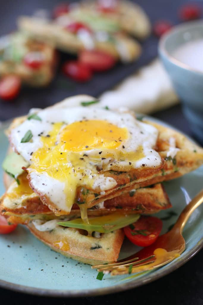 waffles made with egg and cheese stacked on a blue plate and topped with a runny egg 