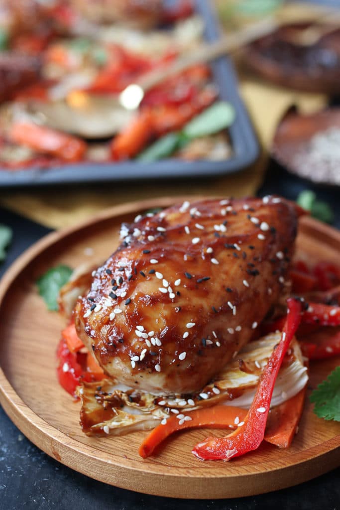 Sticky chicken breast on cabbage and peppers on a wooden plate.