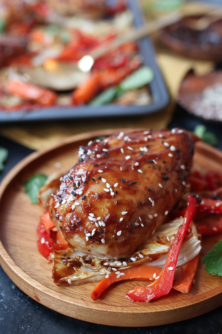 Baked sweet and sour chicken on a bed of cabbage and peppers on a wooden plate.
