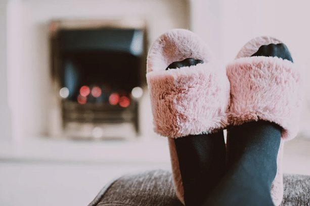 Feet with slippers on in front of a fireplace.