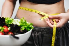 Person measuring their weight circumferance with measuring tape holding a bowl of salad.