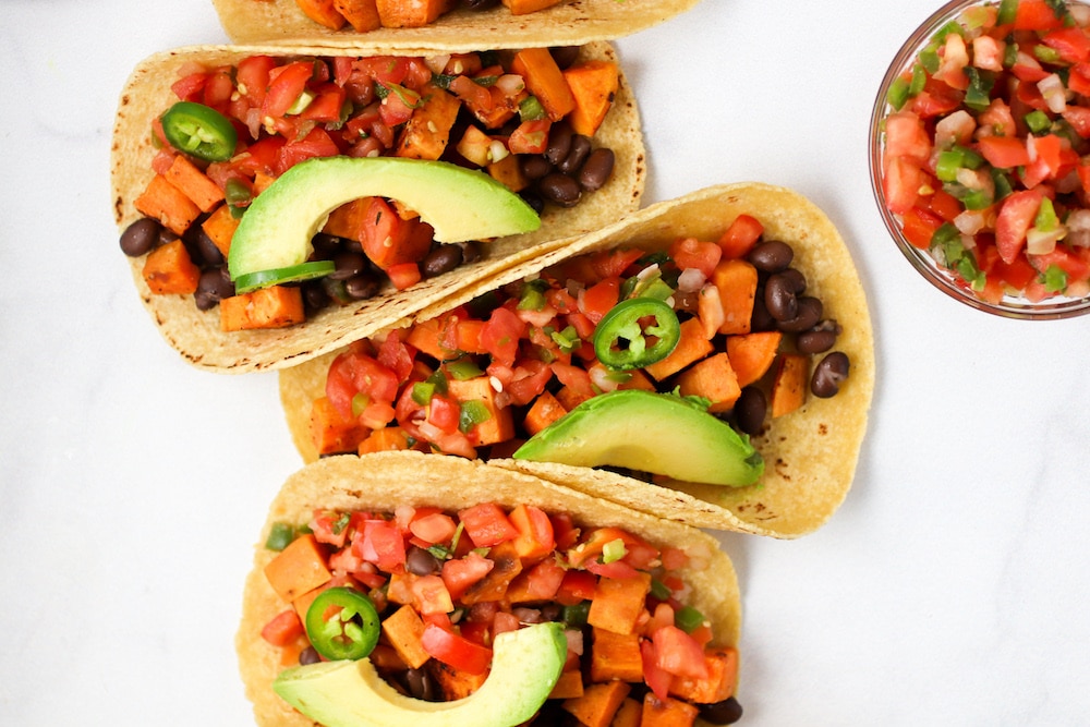 Three sweet potato tacos on a white background topped with a slice of avocado from family meal plan.