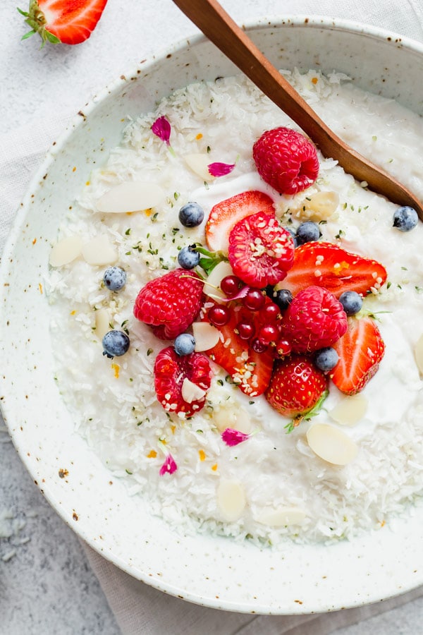 Coconut rice pudding in a white bowl topped with berries and a wooden spoon from family meal plan.