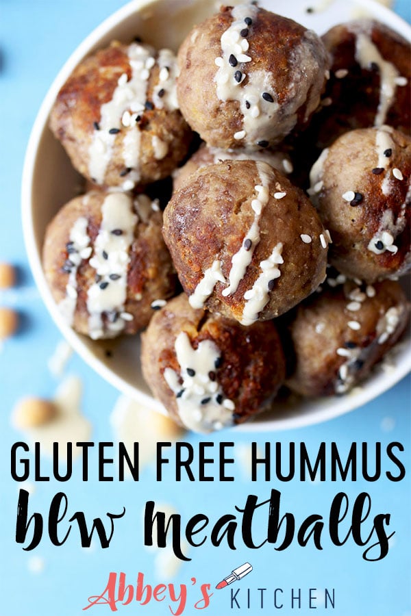 Hummus baby meatballs in a bowl with tahini drizzle and sesame seeds.