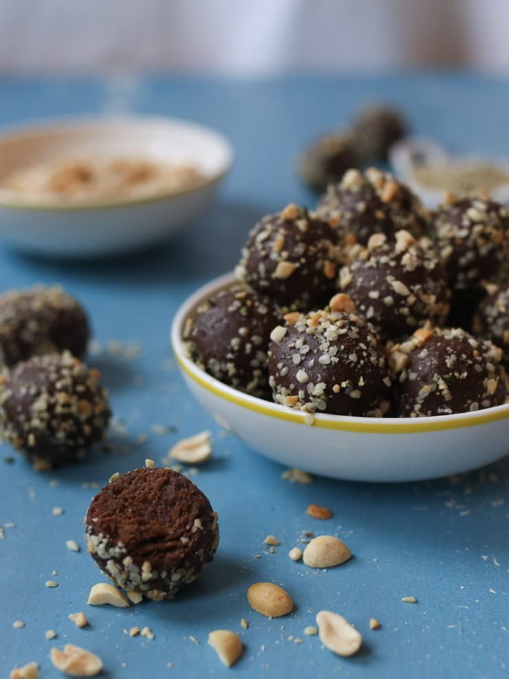 white bowl containing vegan peanut butter chocolate protein balls topped with hemp hearts and chopped peanuts with a white bowl containing additional peanuts in the background on a blue backdrop