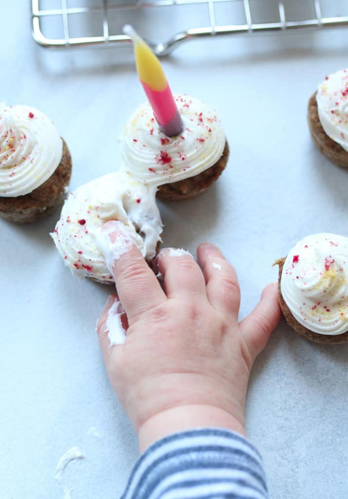 Baby's hand poking at vegan mini birthday cupcakes.