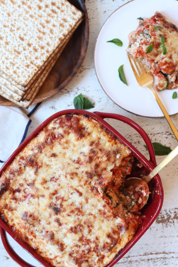 Passover vegetarian lasaga in a red casserole dish next to a serving on a plate.