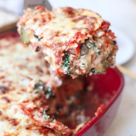 Spatula lifting a piece of vegetarian matza lasagna from a red casserole dish for Passover.