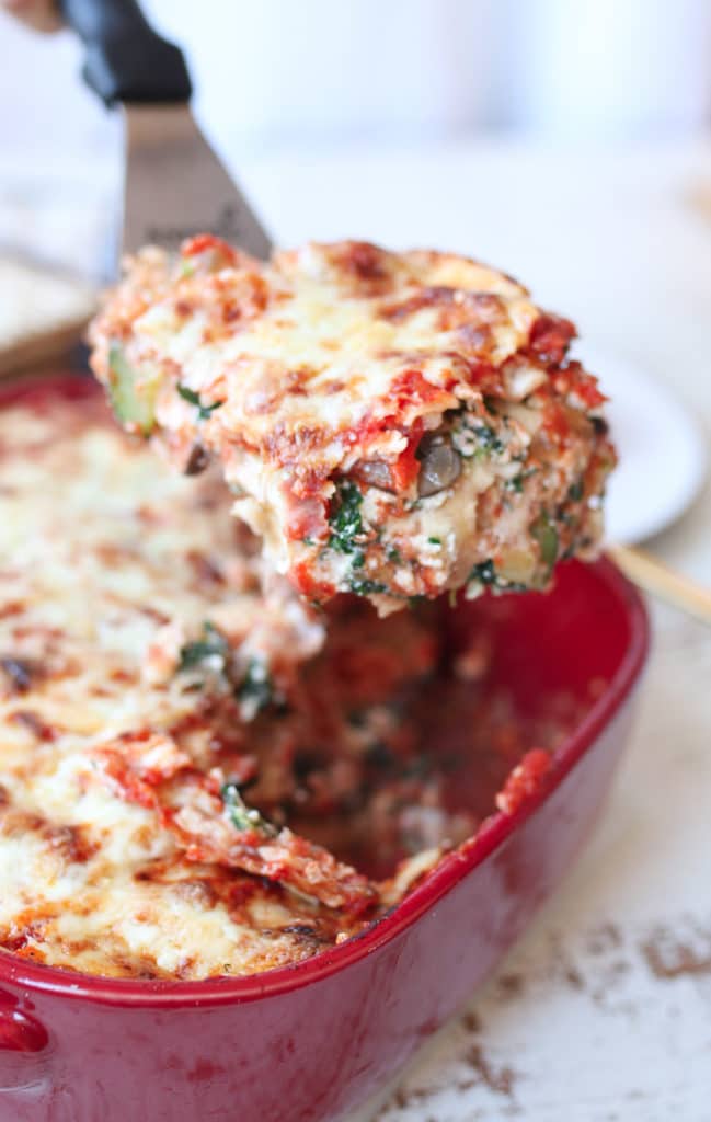 close up image of a spatula holding a piece of vegetarian matzo lasagna for passover out of a red casserole dish