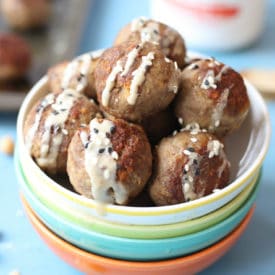 Hummus baby meatballs in a bowl with tahini drizzle and sesame seeds.