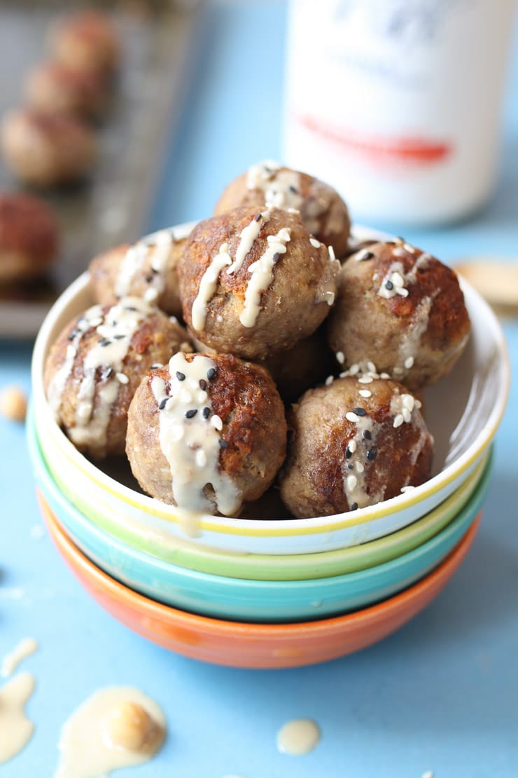 Hummus baby meatballs in a bowl with tahini drizzle and sesame seeds.