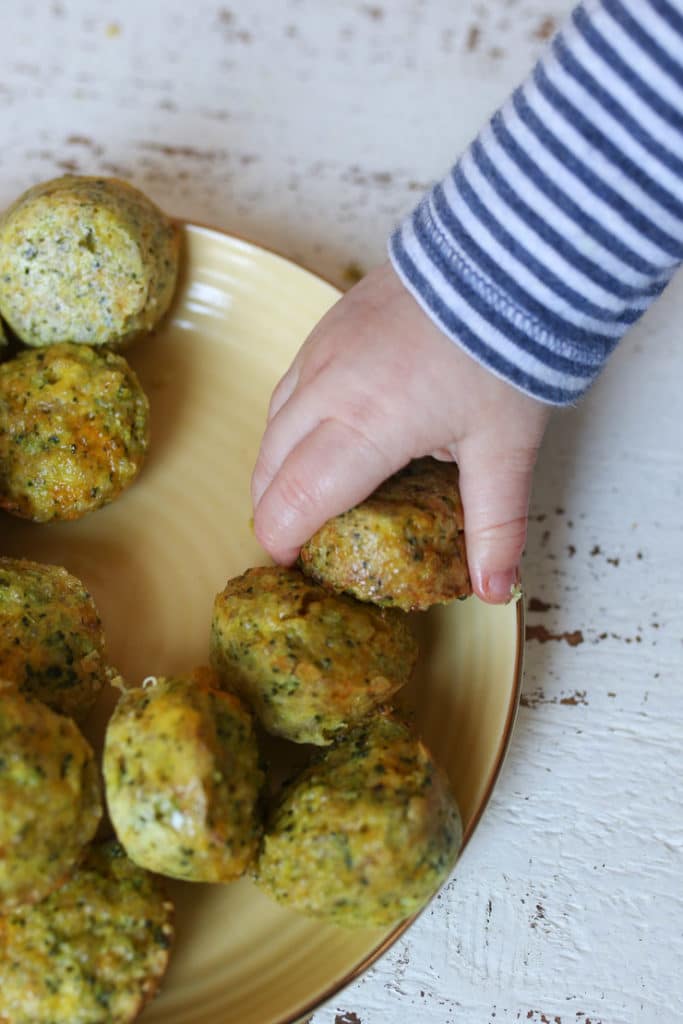 Baby's hand reaching for a mini broccoli and cheese egg muffins.