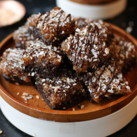 Samoa girl scout vegan brownies on a wooden plate topped with chocolate and coconut.