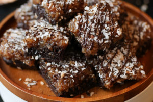 Samoa girl scout vegan brownies on a wooden plate topped with chocolate and coconut.