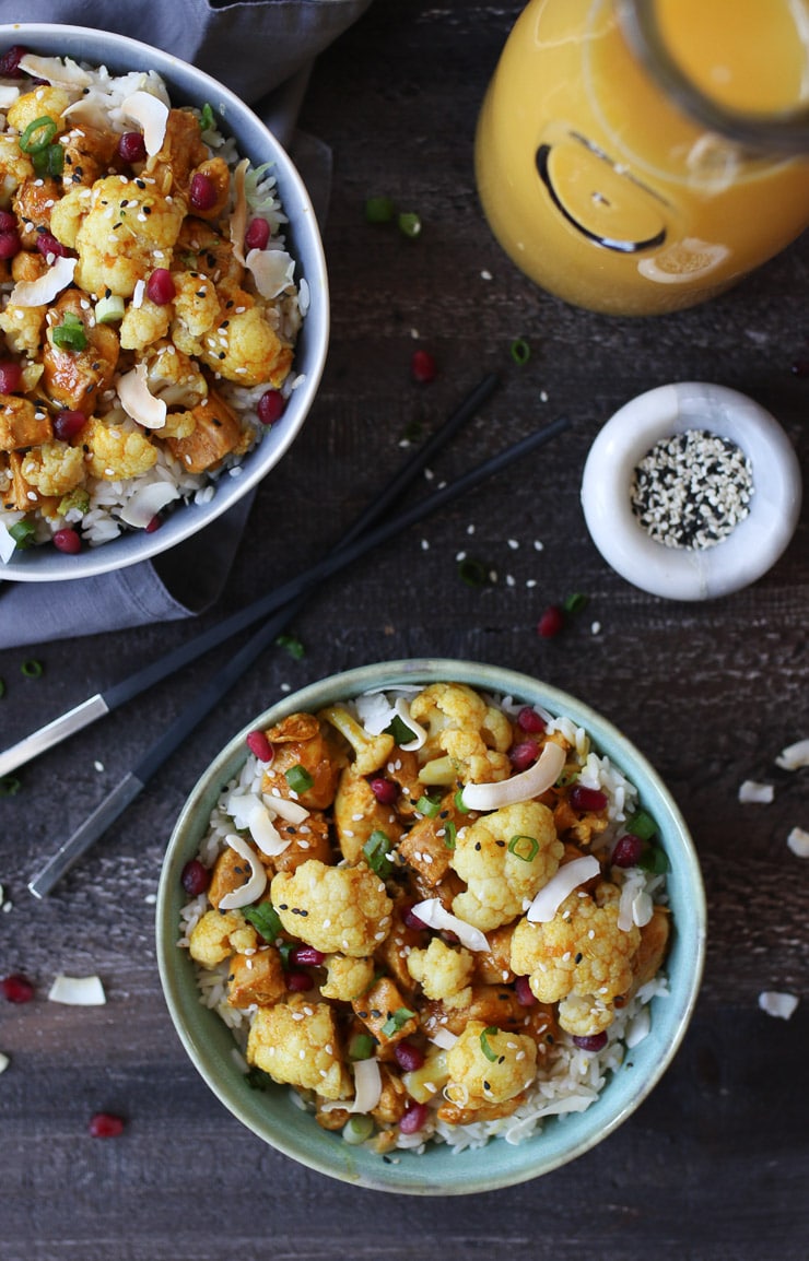 Birds eye view of bowl made with cauliflower, chicken, and florida OJ with orange juice and sesame seed in the background. 