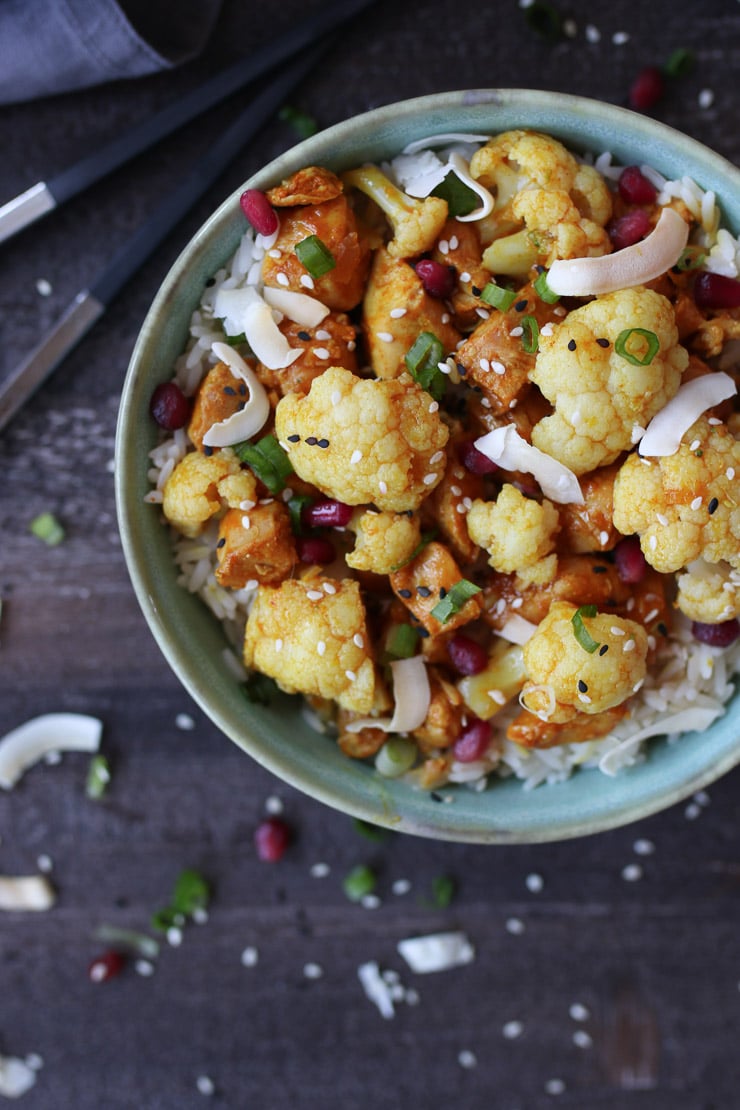 Birds eye view of instant pot orange chicken and cauliflower in a blue bowl garnished with toasted coconut and green onions.