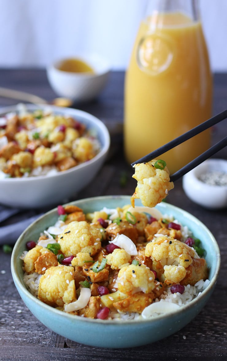 Close up of chop sticks scooping up cauliflower from orange chicken bowl with Florida OJ in the background.