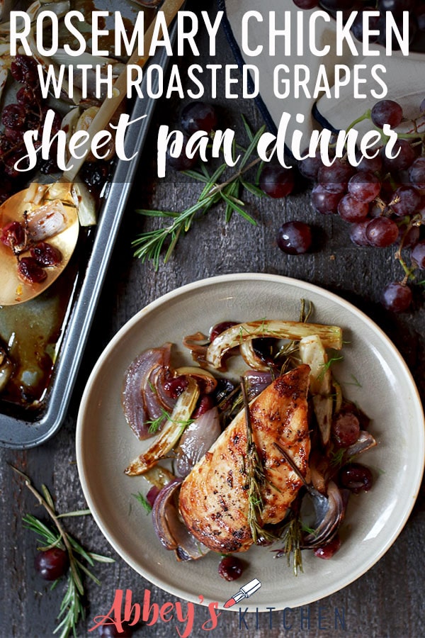 Baked rosemary chicken on a plate with roasted onions and grapes.