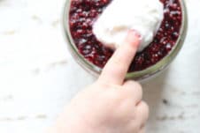 Baby's finger next to vegan chia pudding in a small mason jar.