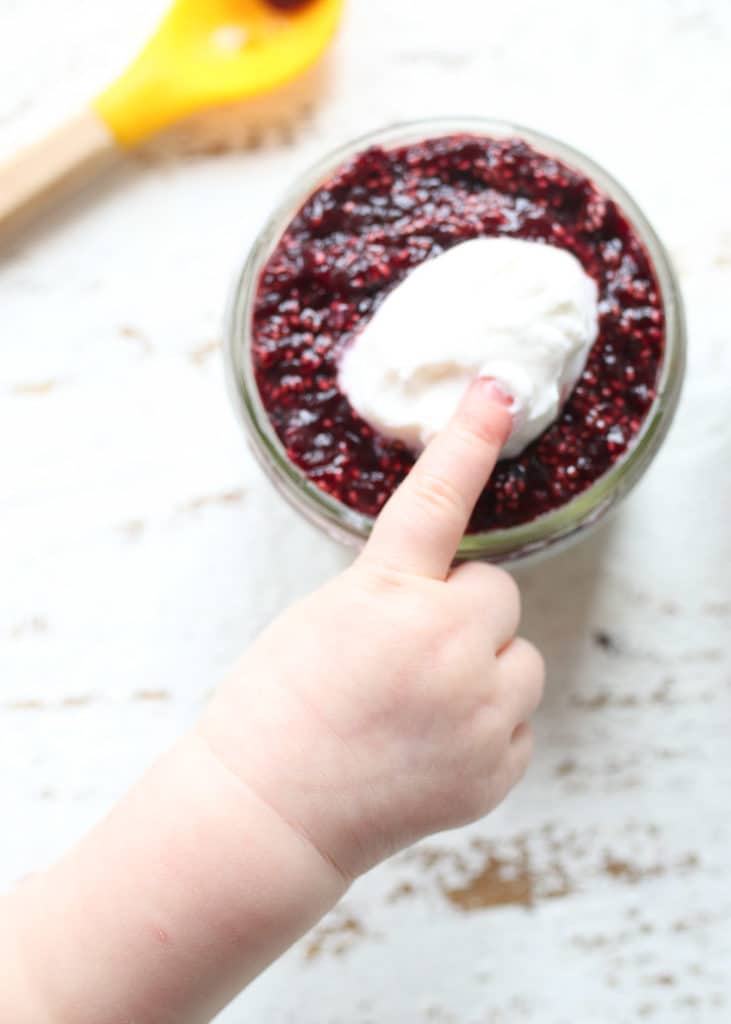 Baby's finger next to vegan chia pudding in a small mason jar.