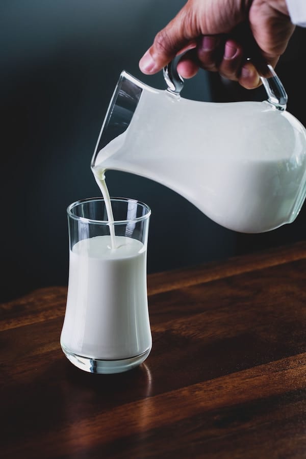 Person pouring a jug of milk into a cup. 