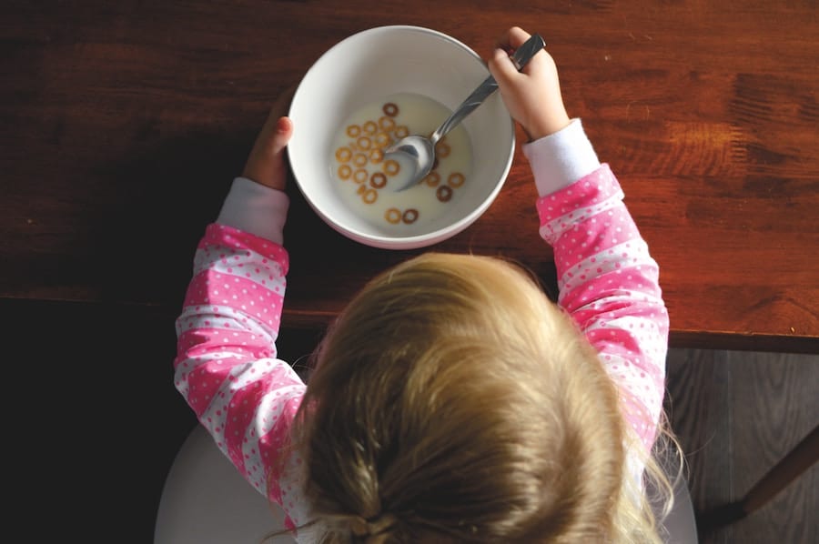 Little girl eating cereal in a bowl.