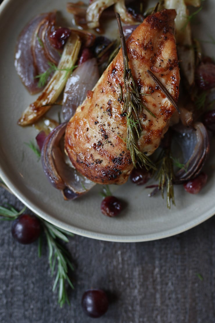 Chicken with balsamic glaze on a plate with roasted onions and grapes.