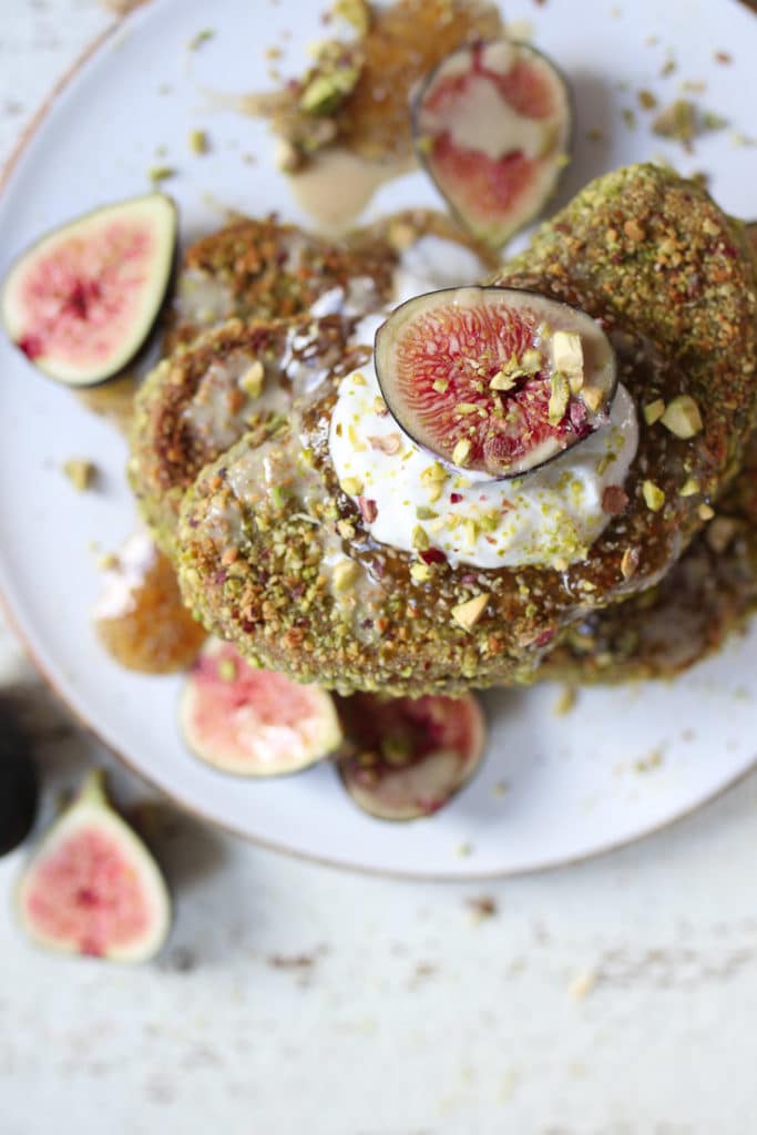 Pistachio crusted french toast on a white plate topped with yogurt and figs.