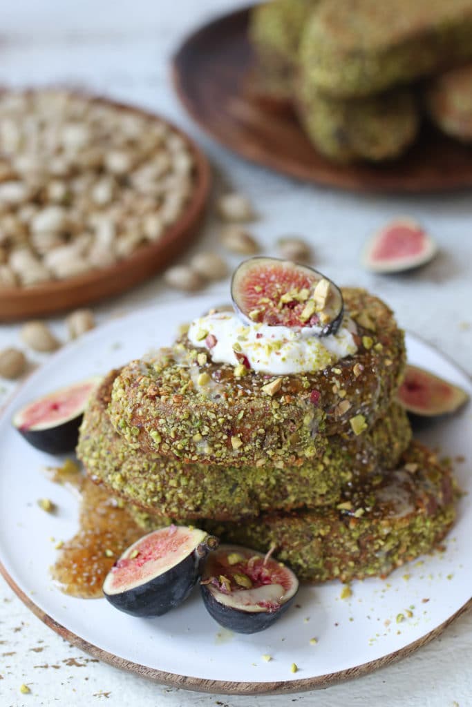 Pistachio crusted french toast on a white plate topped with yogurt and figs.