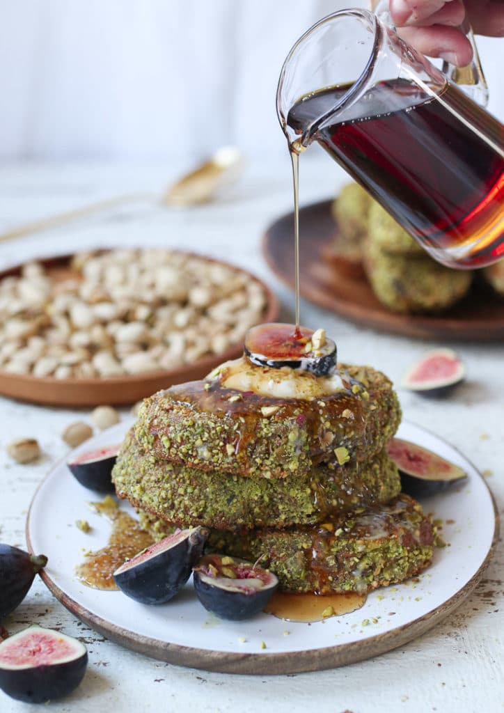 Pistachio crusted french toast on a white plate topped with yogurt and figs.