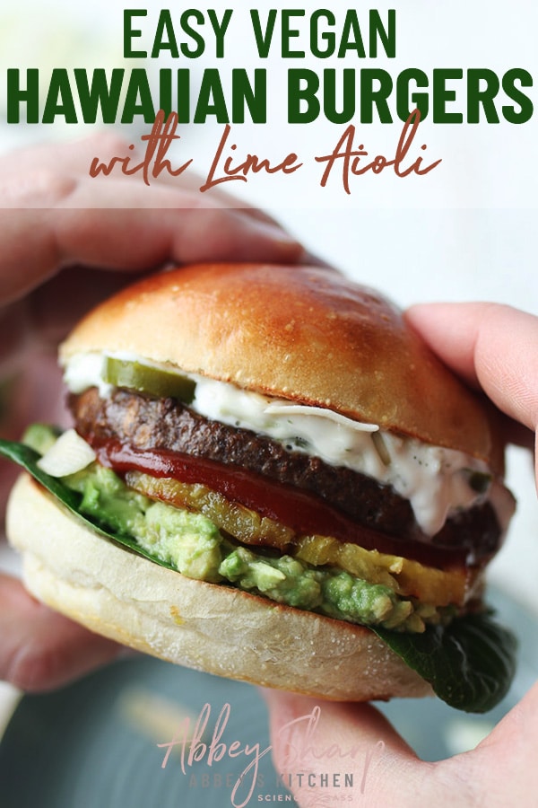 pinterest image of two hands holding a vegan hawaiian burger with homemade lime aioli garnished with avocado, vegetables, and pineapple on a hamburger bun with text overlay