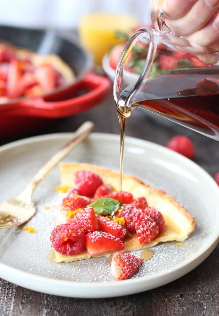 Slice of dutch baby on a plate topped with berries and maple syrup.