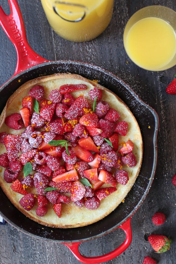 Vegan dutch baby in a pan topped with berries and orange zest.