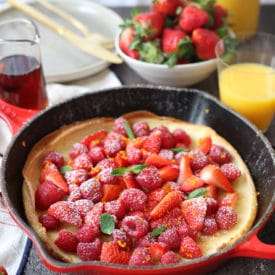 Vegan dutch baby in a pan topped with berries and orange zest.