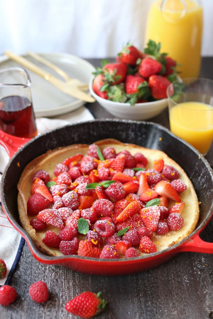 Vegan dutch baby in a pan topped with berries and orange zest.